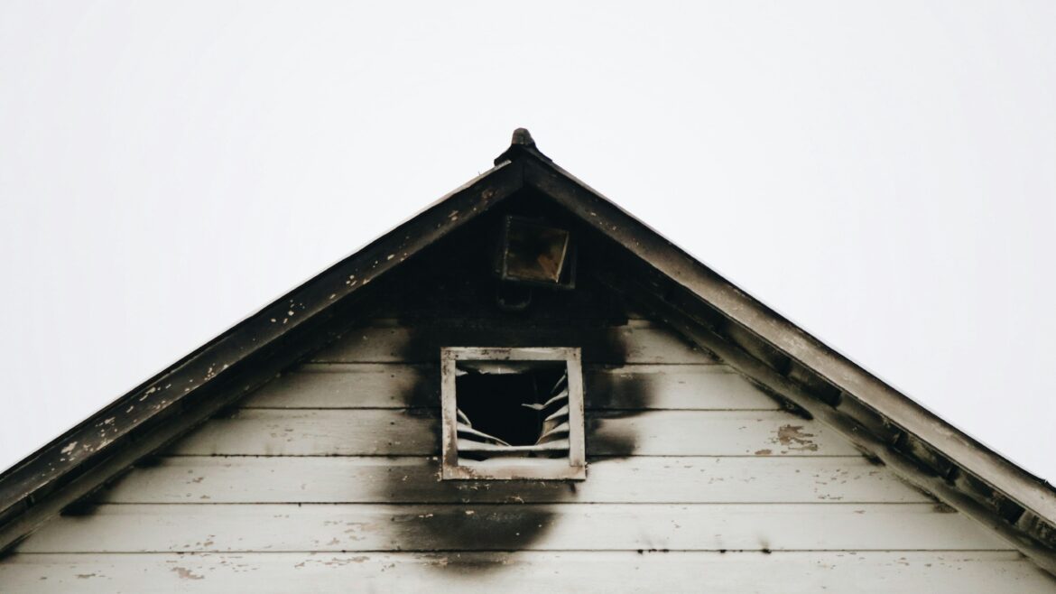 The exterior of a white home with fire damage outside of the attic window