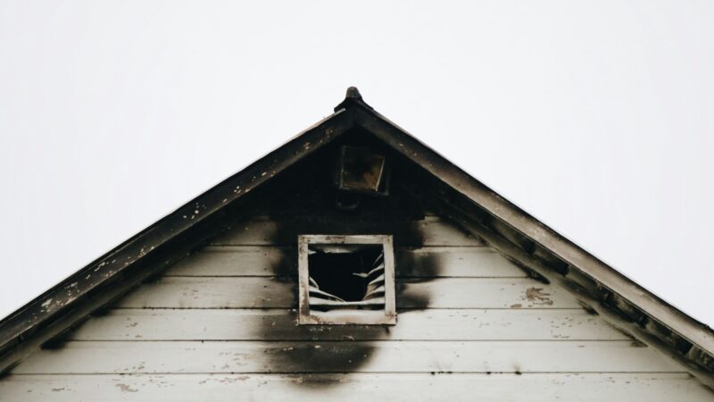 The exterior of a white home with fire damage outside of the attic window